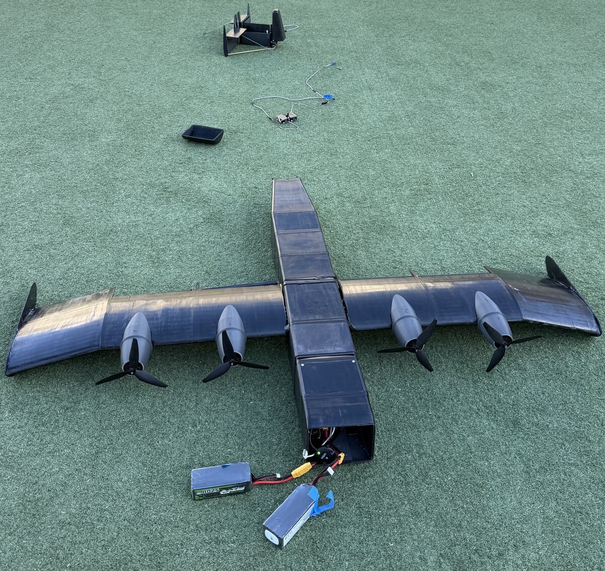 Aftermath of Crash 1: wingbox and tail destroyed, fuselage and wings on the field with battery pack and avionics nearby.